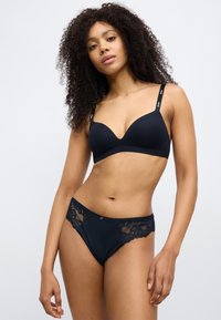 Conjunto de lingerie preta com sutiã moldado e liso, alças ajustáveis e detalhe em renda floral na cueca correspondente. Textura suave em toda a peça.