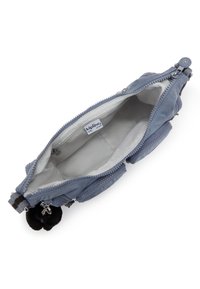 Mała niebieska torba crossbody z otwartą główną komorą, wewnętrzną kieszonką na zamek, przednimi kieszeniami i czarnym pomponem jako breloczkiem na pasku w paski.