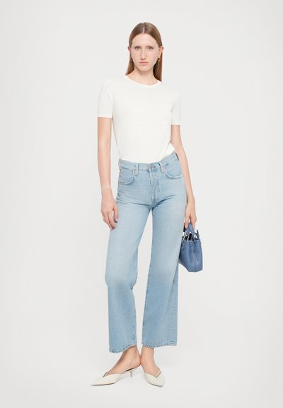 Top bianco a maniche corte, jeans a vita alta larghi di colore azzurro chiaro e décolleté a punta color crema. Include una piccola borsa blu.