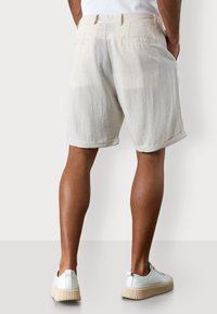 Beige Leinenshorts mit einem lockeren Schnitt, umgeschlagenen Säumen und zwei Gesäßtaschen. Kombiniert mit hellen Sneakers.
