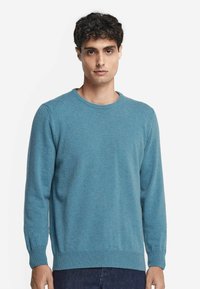 Ljusblått crew-neck tröja gjord av mjukt stickat material. Har långa ärmar, ribbade manschetter och en rak nederkant med en strukturerad yta.