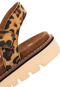 Zamszowy pasek na kostkę w panterkę z zapięciem na rzep na sandałach na platformie z grubą beżową podeszwą i przeszywanym wykończeniem.