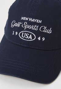 Navy blue baseball cap made of cotton, featuring white embroidered text: "NEW HAVEN GANT SPORTS CLUB USA 1949" on the front.