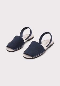 Sandalias de tacón en azul marino, hechas de ante, con diseño de punta abierta, plantilla de cuero beige y suela de goma negra con detalles de costura blanca.