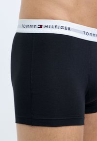 Sorte bomuldsboxershorts med en hvid elastisk talje, der har "TOMMY HILFIGER" logoet. Enkel design med en glat tekstur.