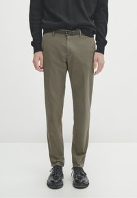 Pantaloni verdi oliva con vestibilità slim, realizzati in morbido cotone, caratterizzati da una cintura semplice e abbinati a scarpe in pelle nera.