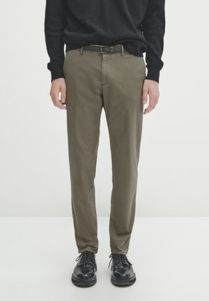 Pantaloni verdi oliva con vestibilità slim, realizzati in morbido cotone, caratterizzati da una cintura semplice e abbinati a scarpe in pelle nera.