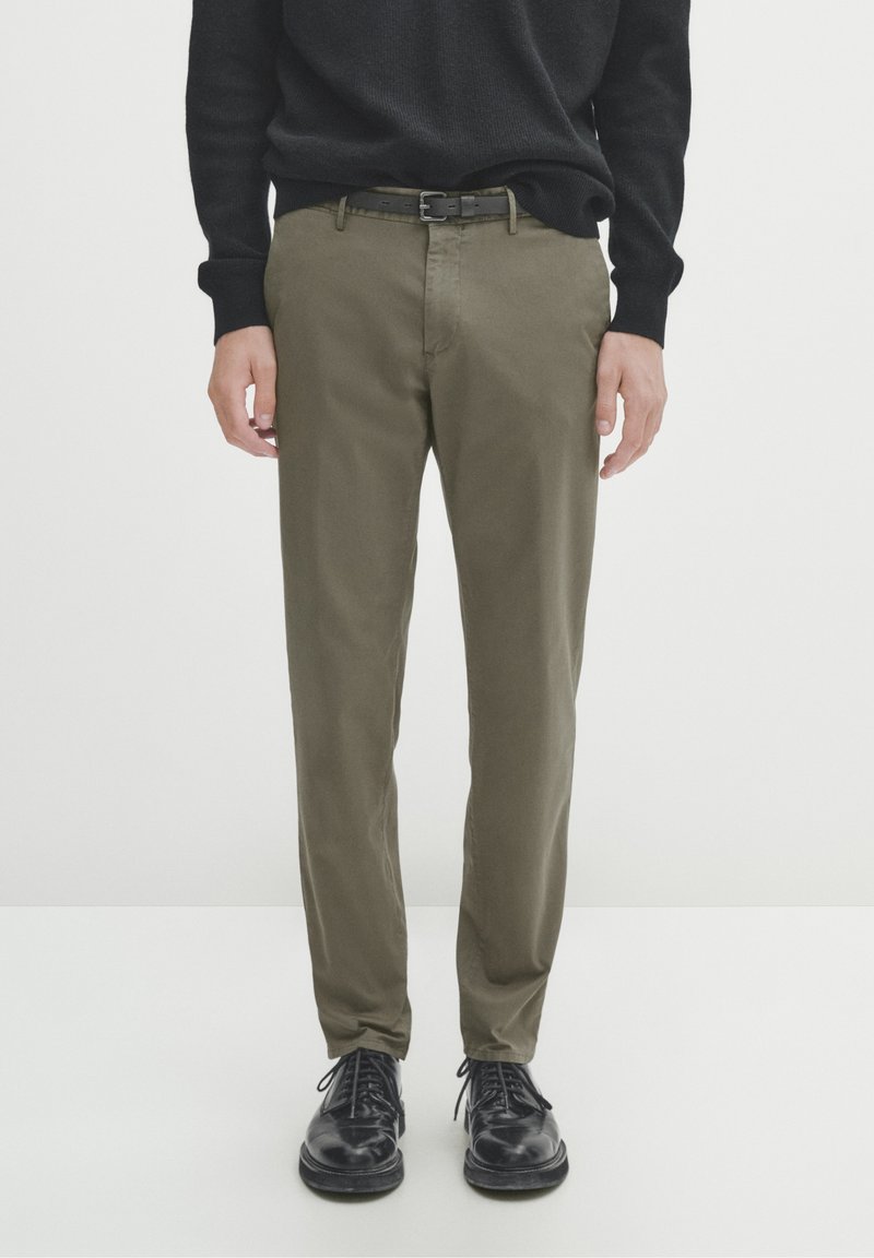 Pantaloni verdi oliva con vestibilità slim, realizzati in morbido cotone, caratterizzati da una cintura semplice e abbinati a scarpe in pelle nera.