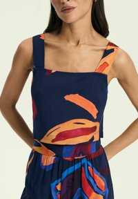 Granatowa bluzka z kwadratowym dekoltem i szerokimi ramiączkami, ozdobiona kolorowym, abstrakcyjnym wzorem w odcieniach pomarańczowego, czerwonego i niebieskiego na lekkim materiale.