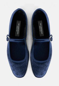 Zapatos Mary Jane de terciopelo azul marino con punta redondeada, suela plana y una correa con hebilla metálica en el empeine. Interior de textura suave.