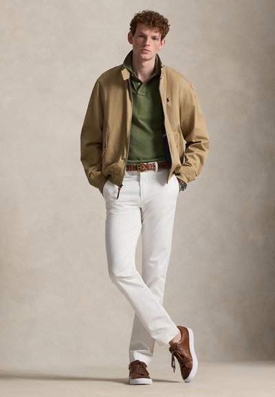 Kevyt vaaleanruskea pommitakki tummanvihreän poolopaidan, valkoisten housujen ja ruskeiden lenkkareiden päällä. Asusteina on kudotulla kuvioidulla vyöllä ja kellolla.