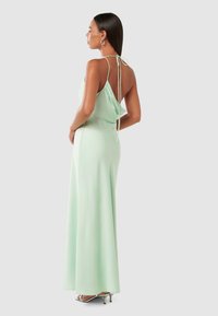 Mint green, long silk dress with a draped back, tied straps, and flowing silhouette. Features a subtle sheen and a minimalist design.