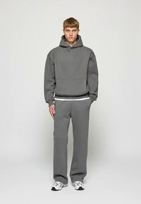 Sweat à capuche gris avec poche avant et pantalon de survêtement gris assorti. Le matériau semble doux ; le design présente une coupe décontractée et une ceinture élastique.