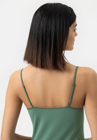 Groene mouwloze top met dunne verstelbare bandjes, met een gladde textuur en een nauwsluitend ontwerp, getoond vanuit de rug.