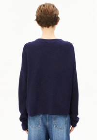 Marineblauer gestrickter Pullover mit langen Ärmeln, Rundhalsausschnitt und gerippter Textur. Der verkürzte Schnitt sitzt über hoch taillierten blauen Jeans.
