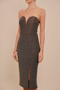 Bezplecu, pieguļošas tumši pelēkas metāliskas auduma kleita. Raksturīga sirds formas kakla izgriezums un priekšējais šķēlums pie ceļa līmeņa.