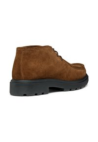 Stivali alla caviglia in suede marrone con punta arrotondata, dotati di suole in gomma nera e dettagli di cucitura discreti, progettati per comfort e supporto.