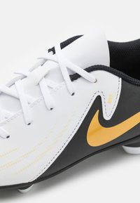 Valkoinen ja musta jalkapallokenkä, jossa on teksturoidusta nahasta valmistettu päällinen, valkoiset nauhat, keltainen Nike-merkki ja muotoillut piikit.
