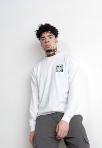 Long-sleeve white T-shirt with a black "OBEY" logo on the chest, paired with grey cargo pants. The fabric appears soft and casual.