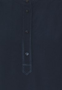 Camicia blu navy con una piastra di bottoni verticale che presenta cinque bottoni e cuciture decorative lungo i bordi.