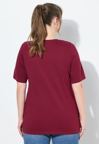 T-shirt corto di colore bordeaux realizzato in tessuto morbido, con scollatura rotonda e vestibilità comoda, abbinato a jeans blu.