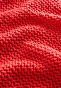 Țesătură tricotată roșie cu un model texturat asemănător cu vafa și fibre moi de lână vizibile.
