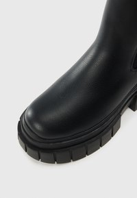 Black leather ankle boot featuring a round toe, textured upper, chunky black rubber sole with pronounced tread, and minimal stitching detail.