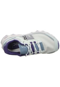 Chaussure de sport bleu clair avec tige en mesh, accents violets et lacets blancs. Dispose d'une semelle coussinée et d'un logo distinctif sur le côté.