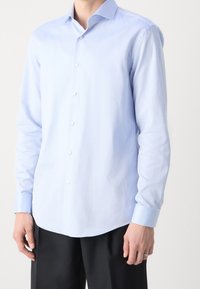 Světlomodrá košile s dlouhým rukávem s texturovaným vzorem, límcem na knoflíky a bílými knoflíky. Tkanina vypadá hladce s mírným leskem.