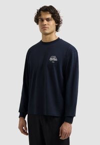 Donkerblauwe langemouwen shirt van een zacht materiaal, met een klein logo op de linkerkant van de borst en een relaxte pasvorm met geribde boorden.