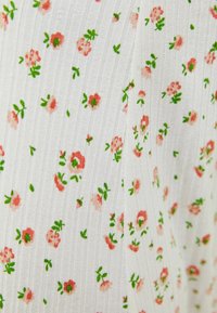 Vit ruggad tyg med små rosa blommor och gröna blad utspridda i ett tätt mönster.