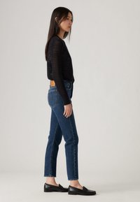 Top de malha preta de manga longa com design em rede. Combinado com jeans azuis de cintura alta e mocassins pretos com detalhes texturizados.