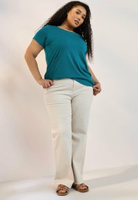 Teal kortärmad t-shirt kombinerad med beige rakbenbyxor och bruna sandaler med vita detaljer. Slätt tyg med avslappnad passform.