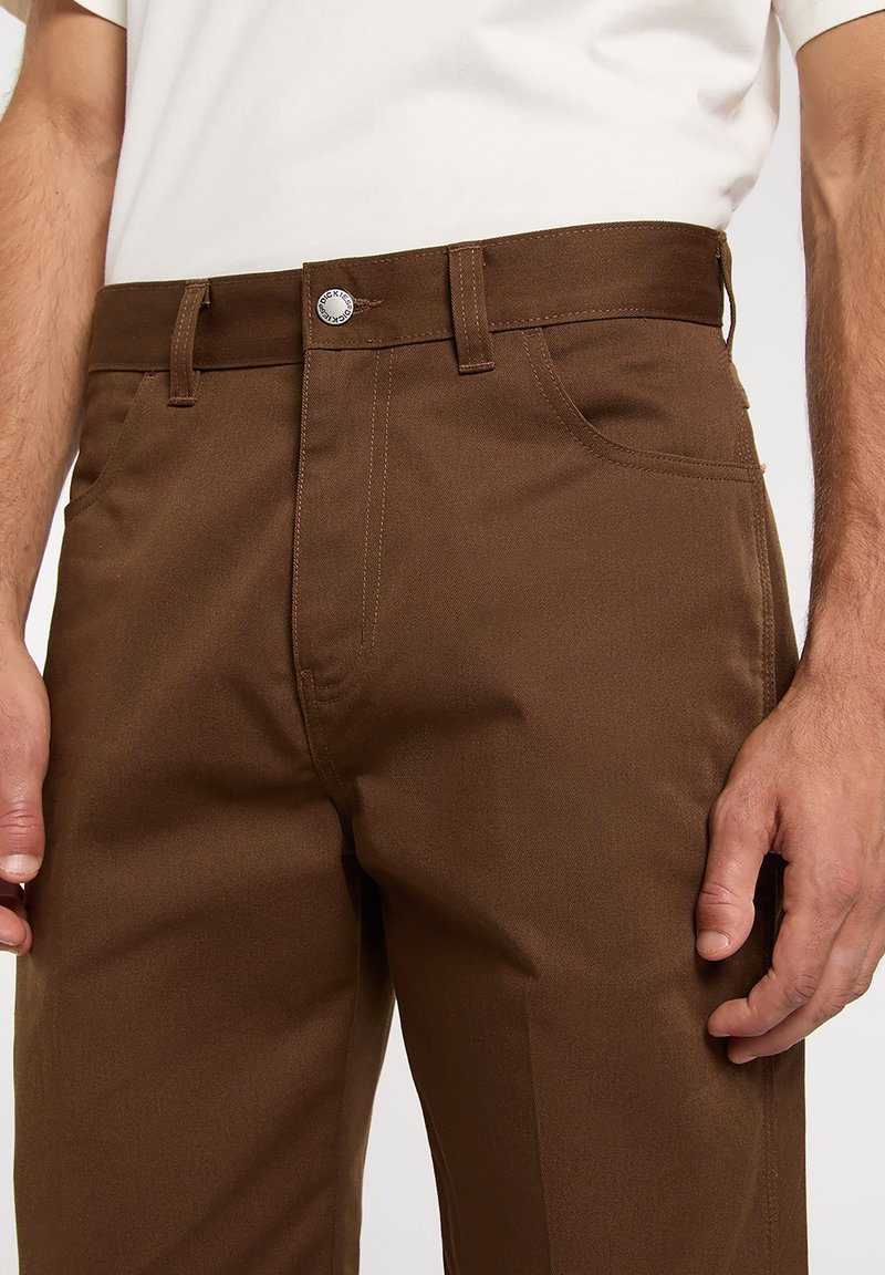 Brown cotton trousers with a straight cut, featuring a metal button closure, belt loops, and side pockets. Smooth texture.