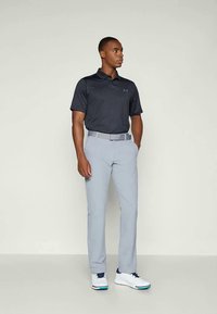 Polo noir à rayures, pantalon gris clair et baskets blanches. Lignes épurées, bien ajusté, avec une marque subtile sur le polo et la ceinture.