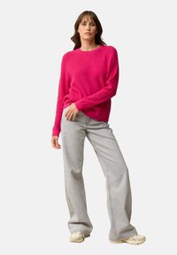 Fuchsia trui met ribbelstructuur, ronde halslijn en een relaxte pasvorm, gecombineerd met lichtgrijze wijde jeans en beige sneakers.