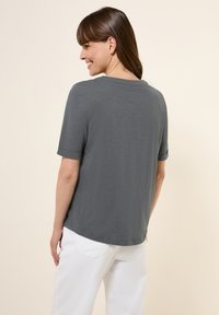 T-shirt gris à manches courtes avec une coupe décontractée, col rond, légère texture et un ourlet qui dépasse la taille, associé à un pantalon blanc.