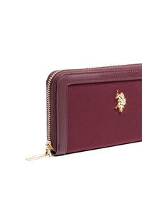 Burgundowy portfel z zamkiem błyskawicznym wykonany z materiału syntetycznego, ze złotymi akcentami i uniesionym logotypem. Gładka faktura z wyraźnymi liniami.