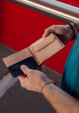 Leather wallet featuring a peach interior, black exterior, multiple card slots, and a snap closure. Logo embossed on the front.