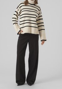 Krämfärgad och svart randig tröja med hög krage och lös passform, i kombination med vida svarta byxor med samlad nederkant.