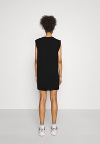 Czarna sukienka bez rękawów o luźnym kroju, z okrągłym dekoltem. Model zestawia ją z białymi i różowymi sneakersami. Gładki materiał, casualowy styl.