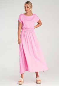 Różowa maxi sukienka z teksturą materiału, krótkimi rękawami i elastycznym pasem w talii. Połączona z sandałami na platformie z plecionym akcentem.