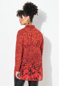 Blusa roja con lunares negros y estampados florales, de manga larga, diseño con cuello, fabricada en tejido ligero, cae hasta la mitad del muslo.