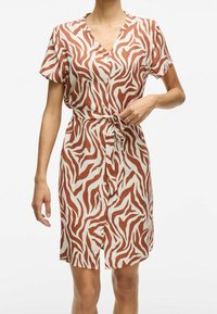 Kortärmad klänning i knä-längd i beige med bruna zebra-ränder. Har en V-ringning och en knutdetalj vid midjan med knappar som prydnad.