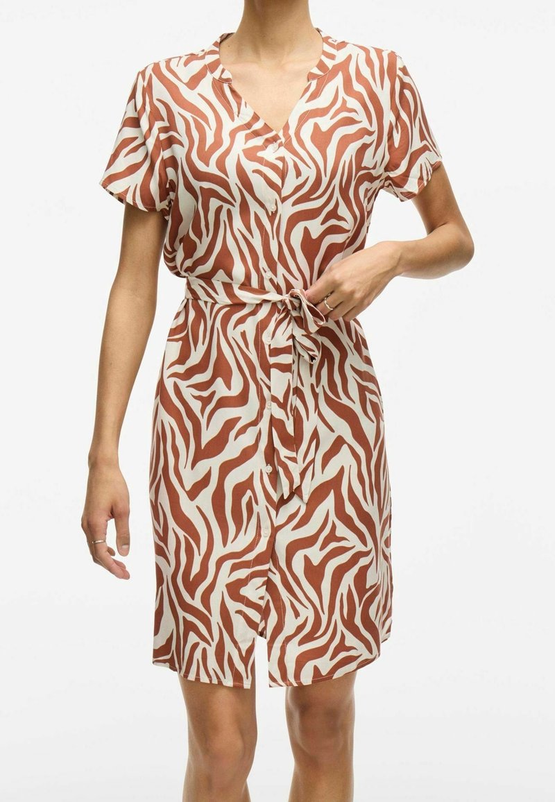 Kortärmad klänning i knä-längd i beige med bruna zebra-ränder. Har en V-ringning och en knutdetalj vid midjan med knappar som prydnad.