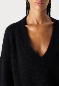 Schwarzer V-Ausschnitt-Pullover mit einer weichen, flauschigen Textur. Verfügt über eine lockere Passform und einen überschnittenen Schulterbereich, was ein entspanntes Design betont.