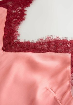 Le tissu en satin rose présente une bordure en dentelle rouge le long de l'encolure. La dentelle a un motif floral avec des bords festonnés, créant un détail texturé.