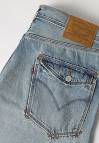 Ανοιχτό μπλε τζιν Levi's που δείχνει πίσω τσέπη με καπάκι με κουμπί και καφέ δερμάτινη ετικέτα μάρκας στη μέση.