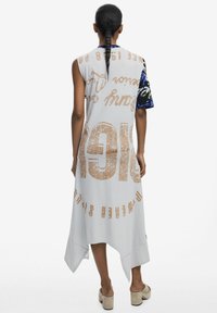 Weißes ärmelloses Kleid mit asymmetrischem Saum, das mit kräftigem braunem Text und mehrfarbigen gemusterten kurzen Ärmeln versehen ist. Glattes, leichtes Material.