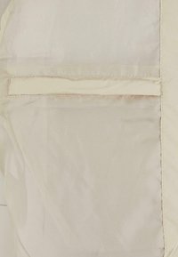 Un tejido beige con una textura suave presenta un bolsillo oculto y costuras decorativas a lo largo de los bordes, creando un diseño elegante y minimalista.